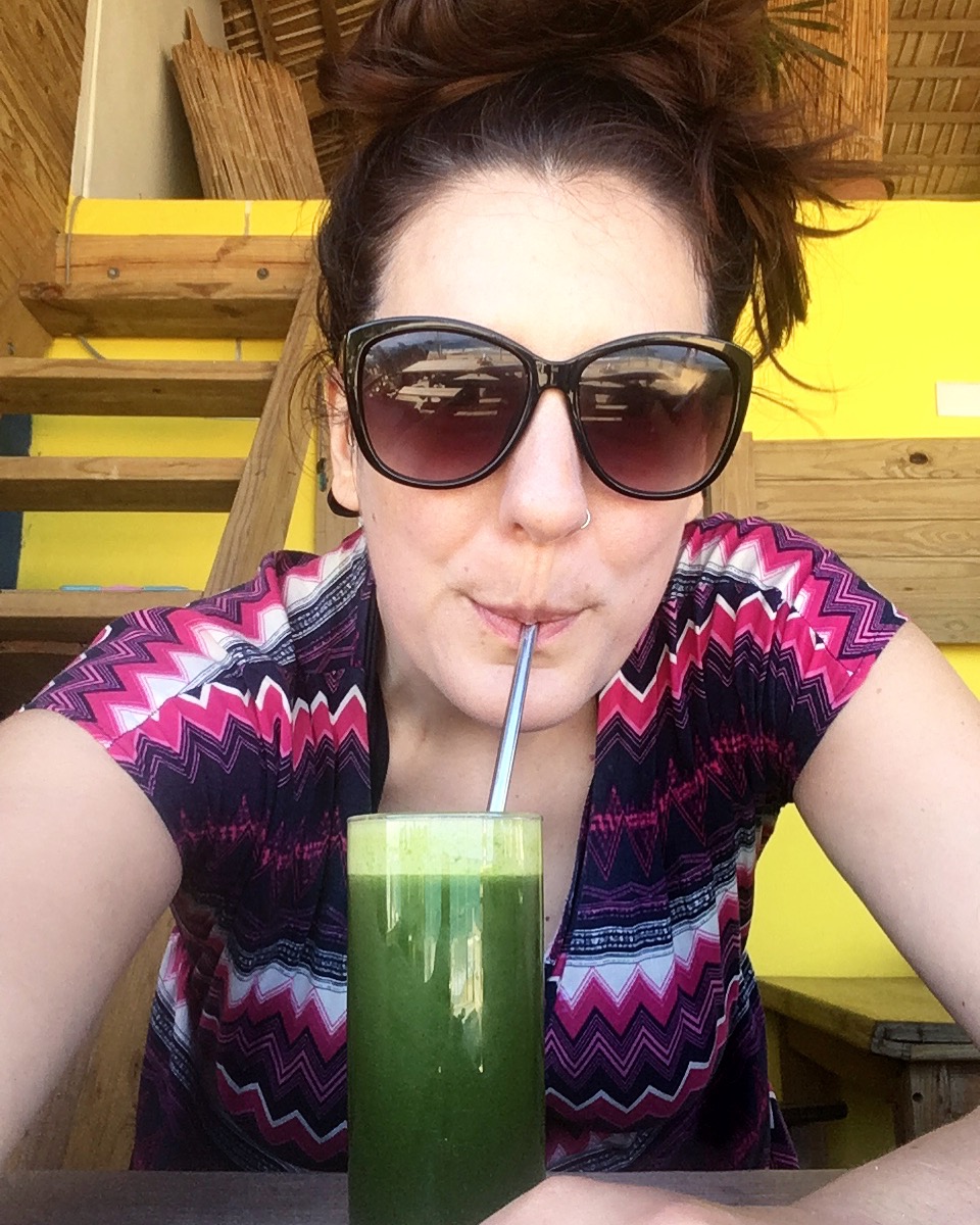 Woman wearing sunglasses and drinking a green juice